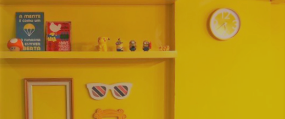 foto de uma parede da agência de publicidade Cubo Amarelo. Ela é toda amarela, com elementos elementos como prateleiras, molduras e relógio no mesmo tom.