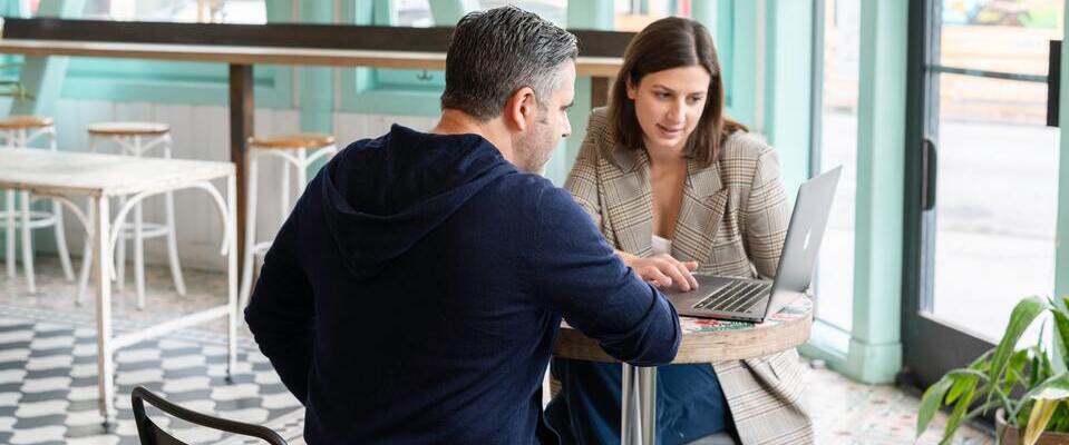 Homem e mulher sentados em uma mesa de café olhando para um computador.