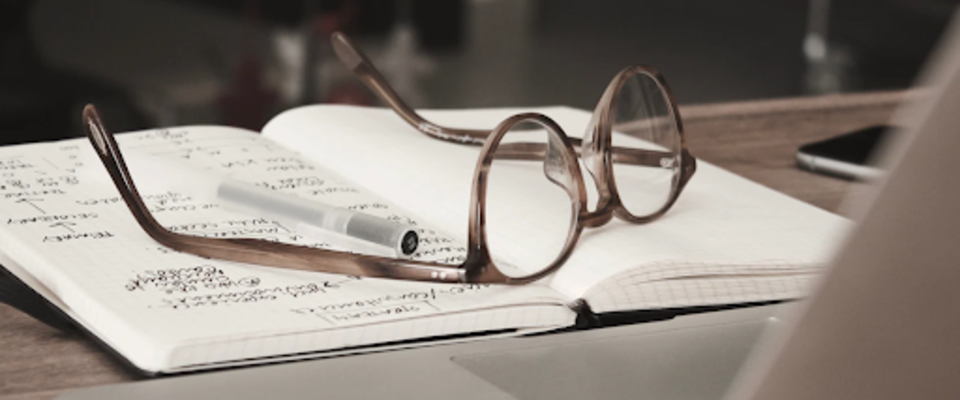Óculos e caneta sobre caderno aberto com anotações
