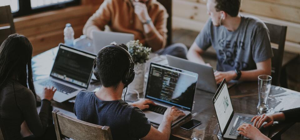 Uma equipe trabalhando e usando computadores ao redor de uma mesa.