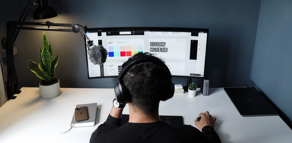 Pessoa de costas, de frente para tela grande de um computador. Nessa tela há paleta de cores e fontes de texto