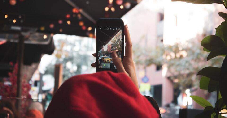 Foto de pessoa de costas fazendo um stories, gravando a rua com um táxi e tempo de outono.