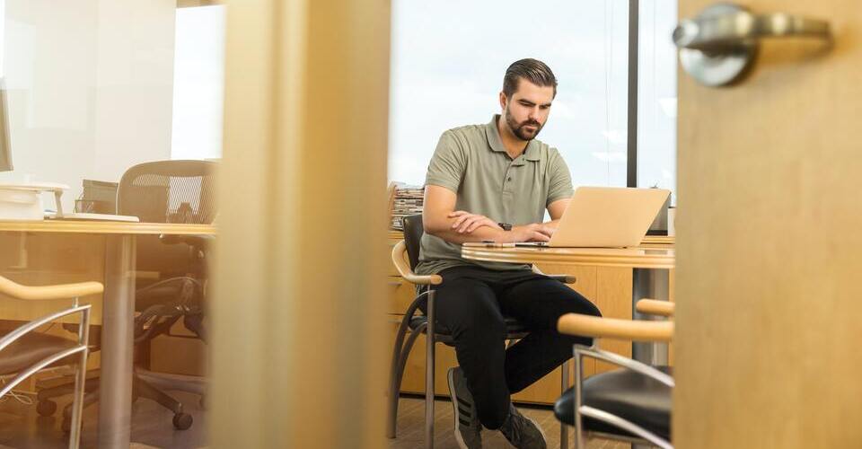 Foto de homem em escritório concentrado enquanto utiliza seu notebook. 