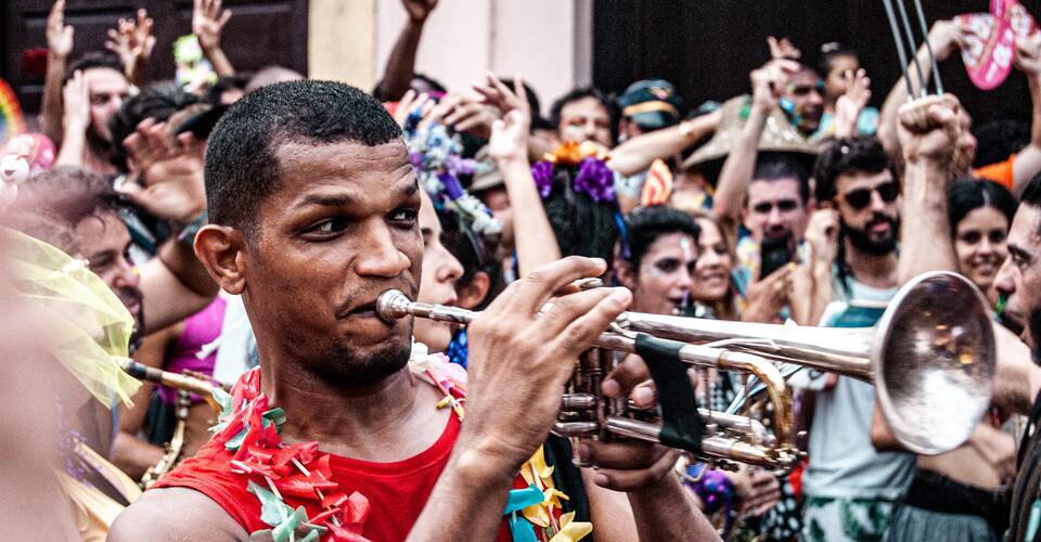 Homem soprando trompete em bloquinho de rua no carnaval. 