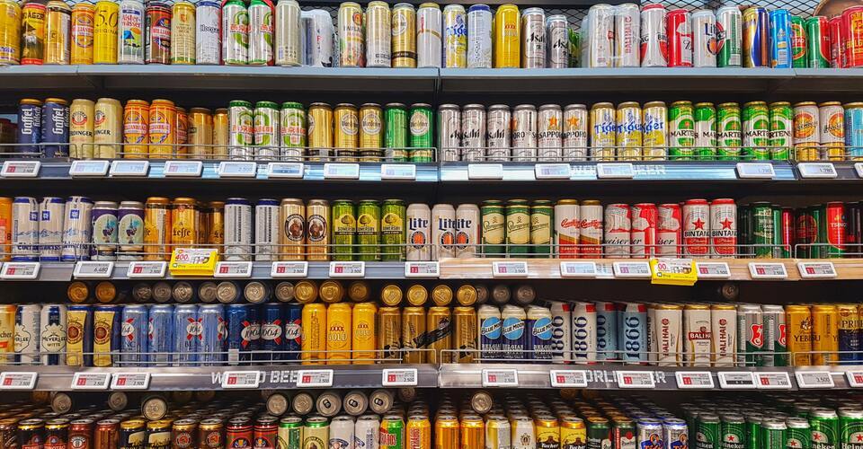 Prateleira de supermercado com várias latas de cerveja.