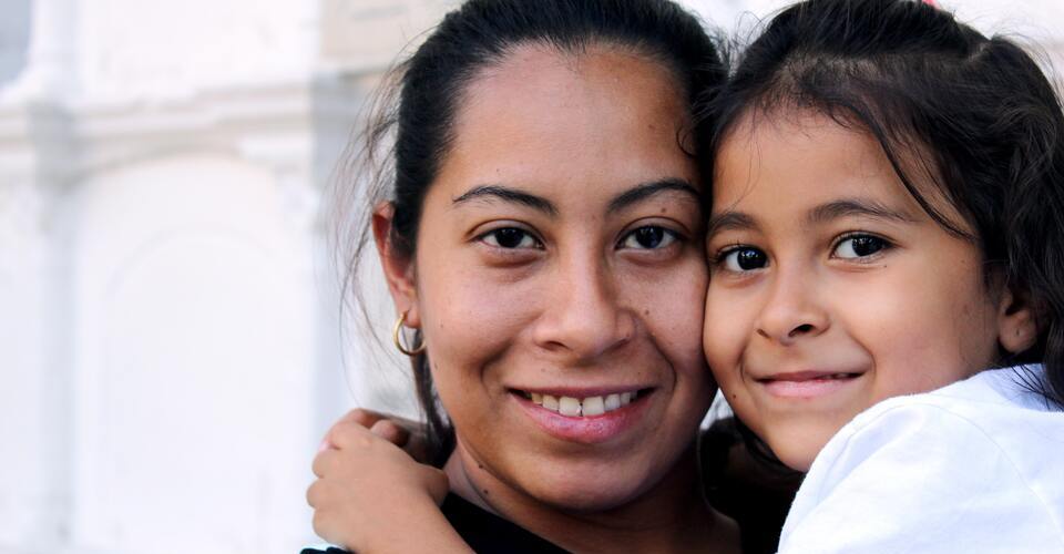 Mãe e filha abraçadas olhando para a câmera. 