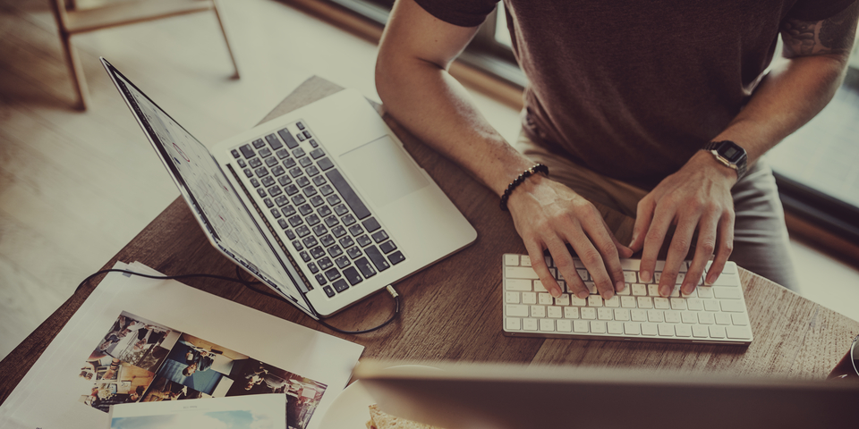 Homem trabalhando com um computador aberto e teclado ao lado.