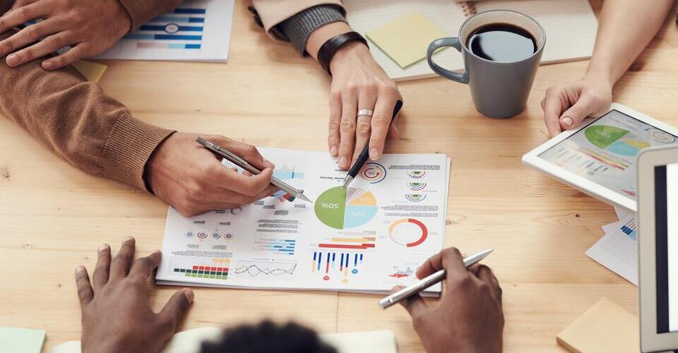 Várias pessoas em volta de uma mesa analisando gráficos impressos em uma folha de papel.