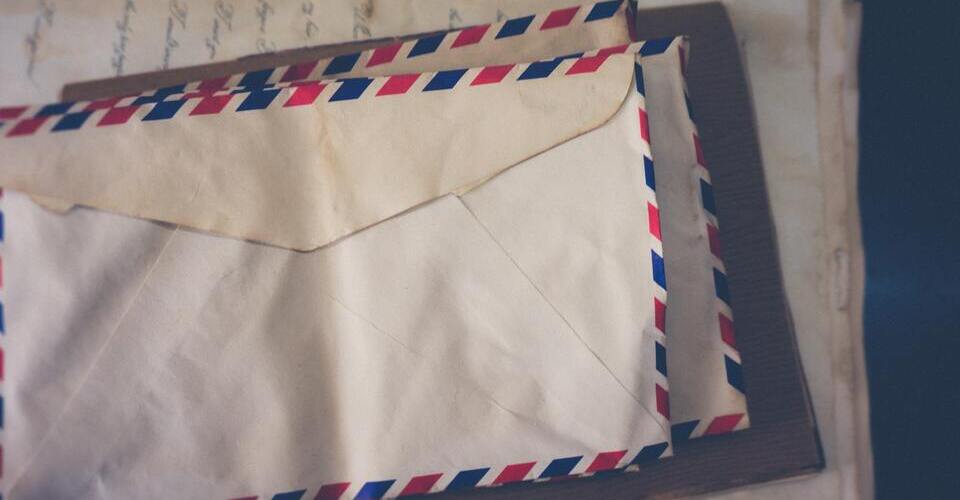 Dois envelopes antigos com bordas azuis e vermelhas. Atrás, papéis com escrita à mão. 