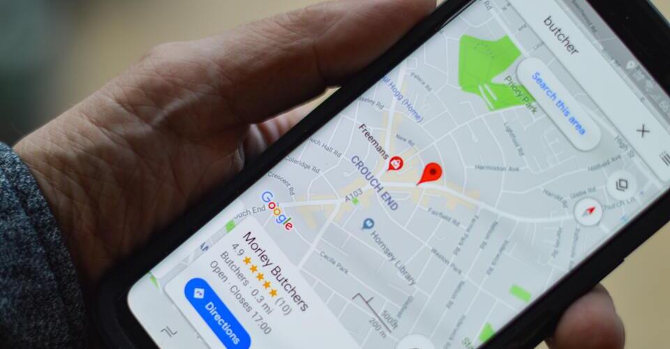 Mão segurando um celular com o Google Maps aberto em uma pesquisa de SEO local.