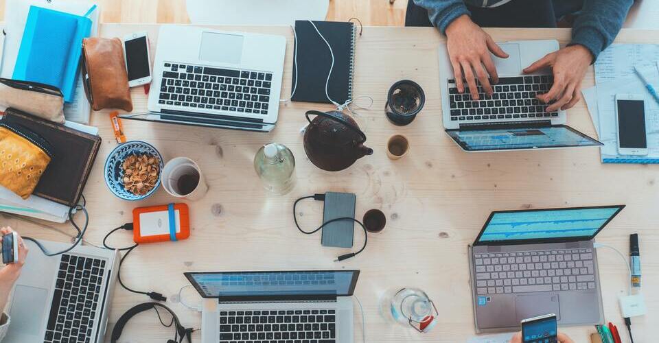 Computadores de uma equipe de trabalho reunidos em uma mesa com outros eletrônicos.