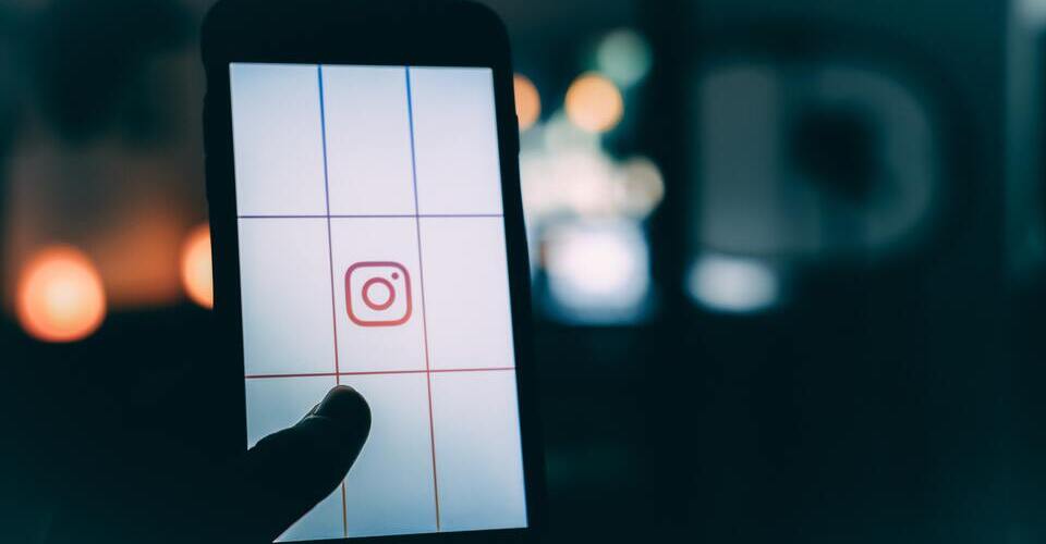 Pessoa segurando celular com a tela dividida em seções. No meio, a logo do Instagram. 