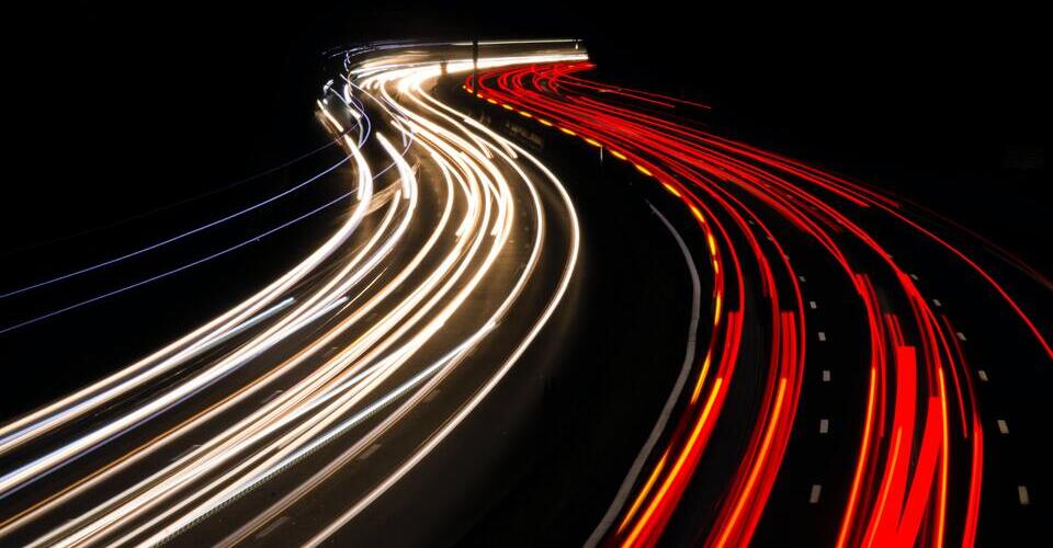 Imagem de longa exposição mostrando faróis de carros em rodovia movimentada.