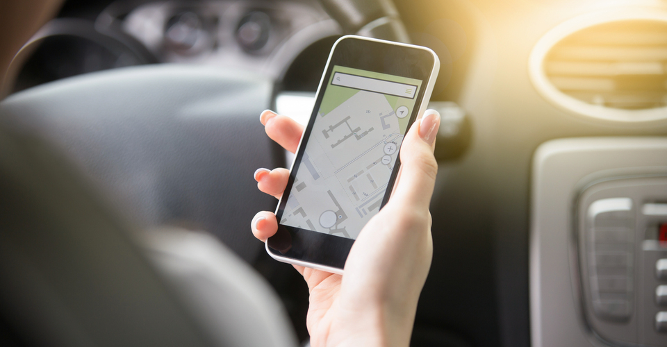 Pessoa usando o celular enquanto dirige para ver trajeto em aplicativo semelhante ao Waze.