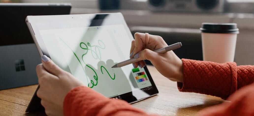 Pessoa desenhando linhas em tablet Surface em cima de uma mesa de madeira.