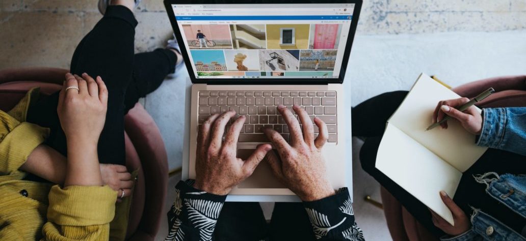 Visão de cima de três pessoas sentadas, uma com computador, outra com caderno, outra com as pernas cruzadas.