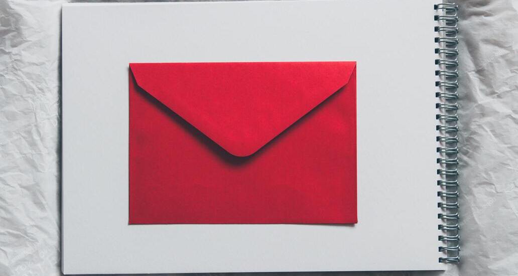 Caderno em branco com envelope vermelho no centro sobre ele.