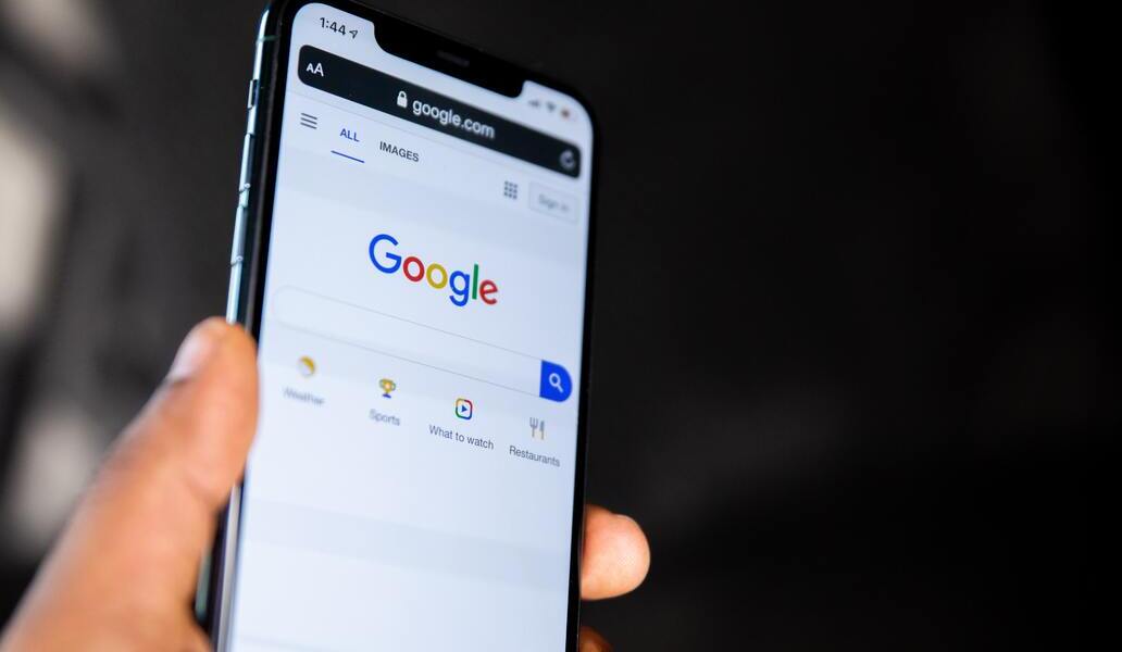 Mão segurando o celular com o site do Google aberto.